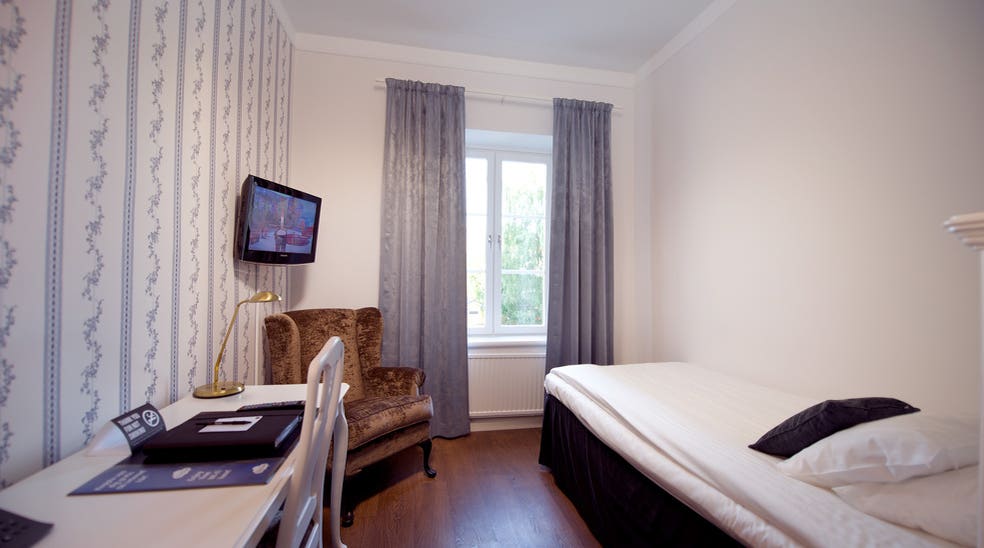 Bright single hotel room with a desk and TV at Bergmestaren Hotel in Falun