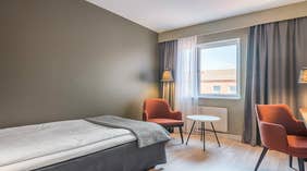 Standard single room with a bed, orange chairs, window, lamp and table at the Quality Hotel Grand Kristianstad