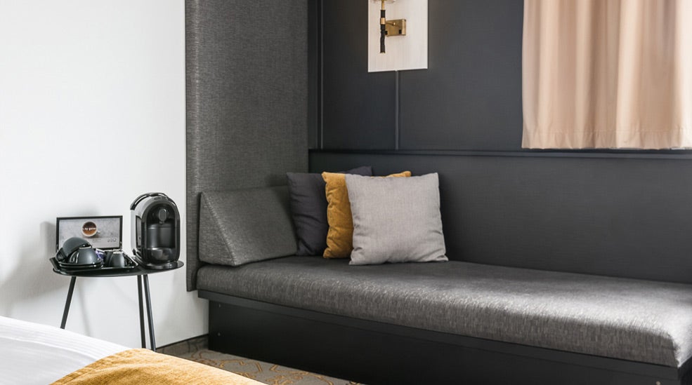 Grey sofa and coffee machine with cups in a deluxe double room at the Quality Hotel Royal Corner